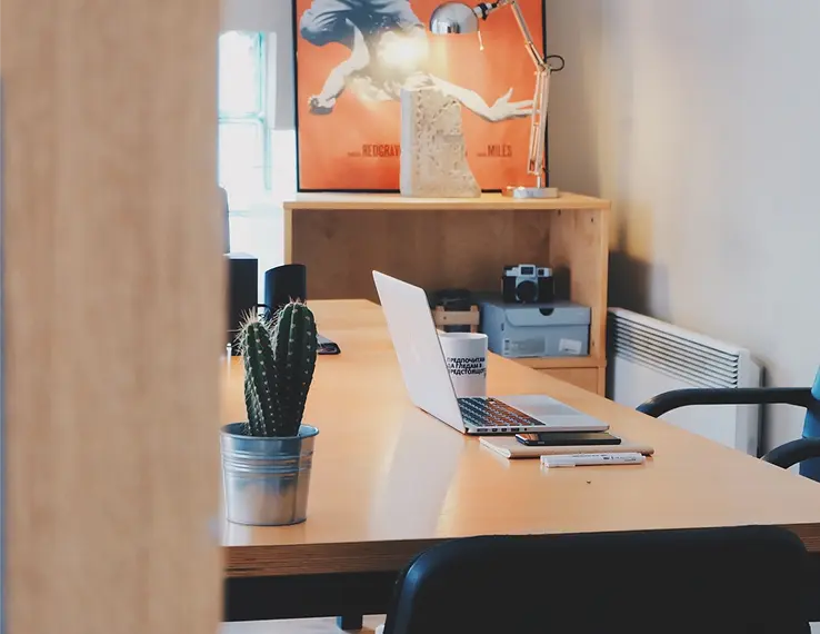 An office desk with a laptop, pens, a cactus, and a camera, with a modern and minimalist design.