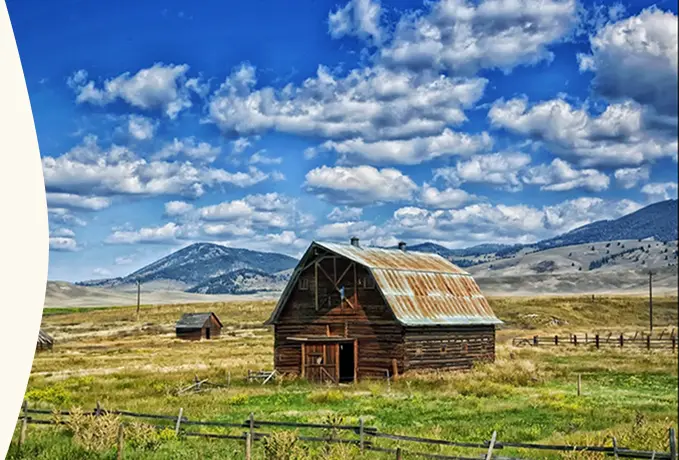 Barn in an open field with rolling hills and cloudy sky in the background.