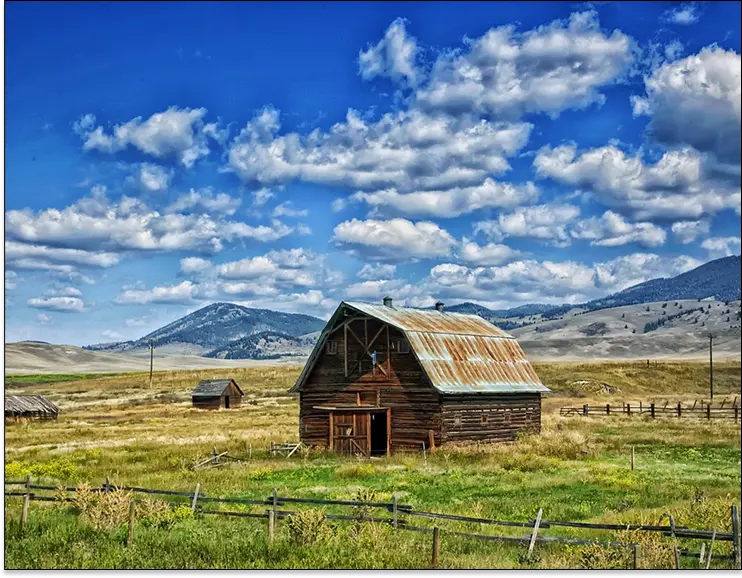 Barn in an open field with rolling hills and cloudy sky in the background.