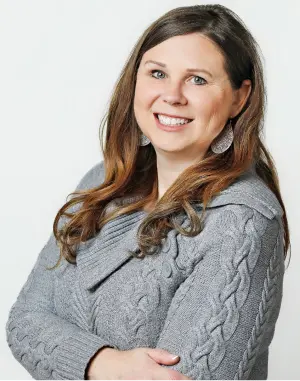 "Professional headshot of Jennifer, wearing a gray sweater, with long hair and earrings, smiling.