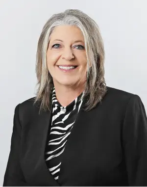 Professional headshot of Karie, wearing a black blazer and zebra print blouse, smiling.