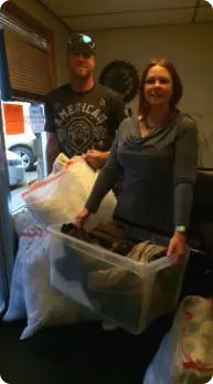 A man and a woman holding bags and a box filled with donations.