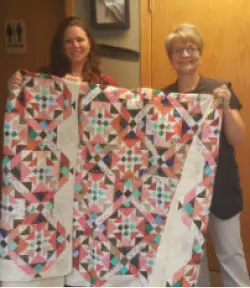 Two women holding up a quilt with colorful geometric patterns.