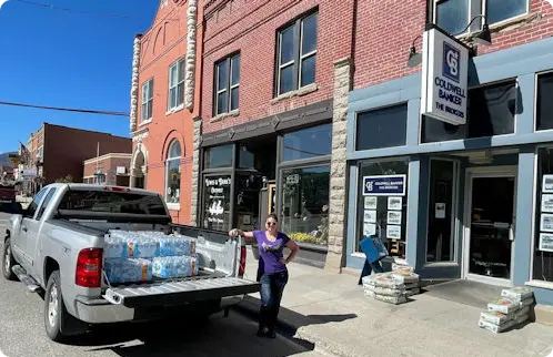 Woman standing beside a truck loaded with water bottles outside the Coldwell Banker building in Red Lodge.