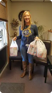 Woman holding two bags of school donations, wearing a blue shirt and brown boots.